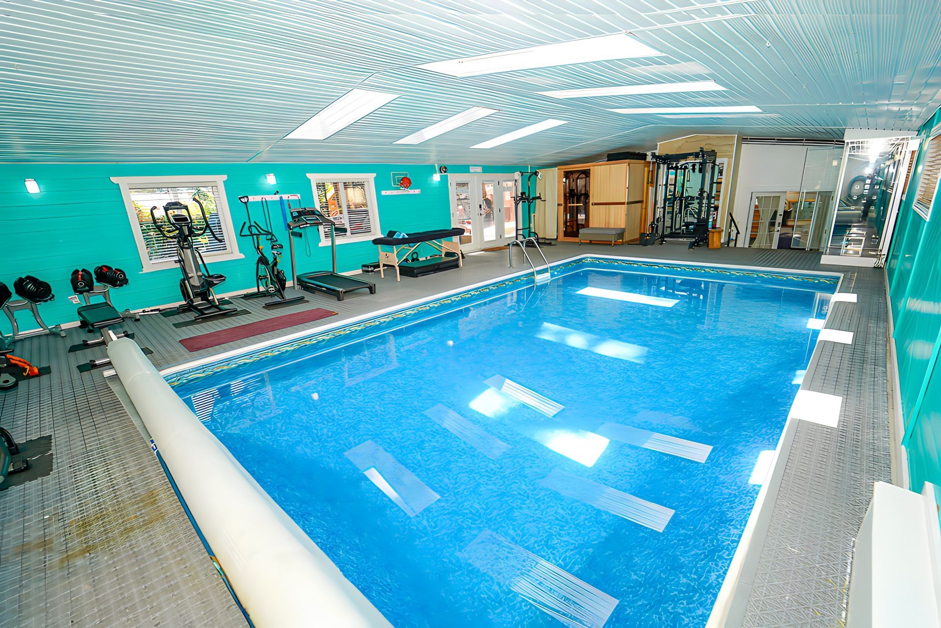Indoor pool and exercise area with turquoise walls, bright blue water, and fitness equipment.