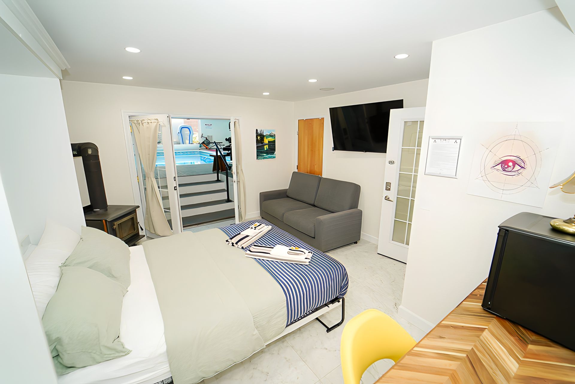 Studio apartment with bed, sofa, TV, and open doors to a pool.