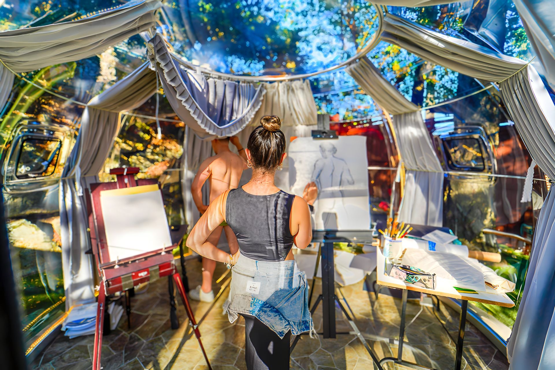 A woman is standing in a tent painting a picture of a man.