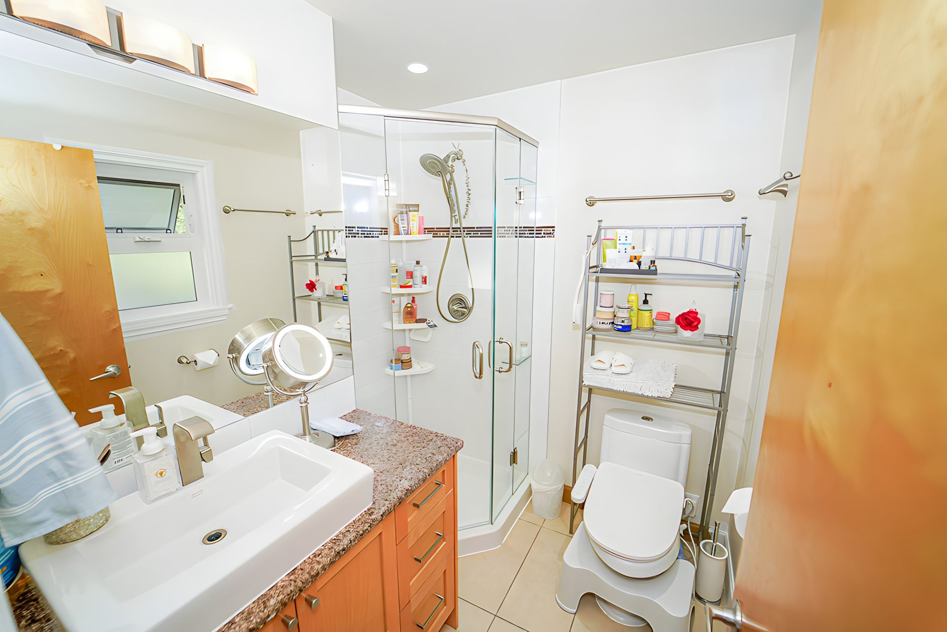 Bathroom with a glass shower, toilet, sink, and storage shelves; tan walls, orange cabinet.