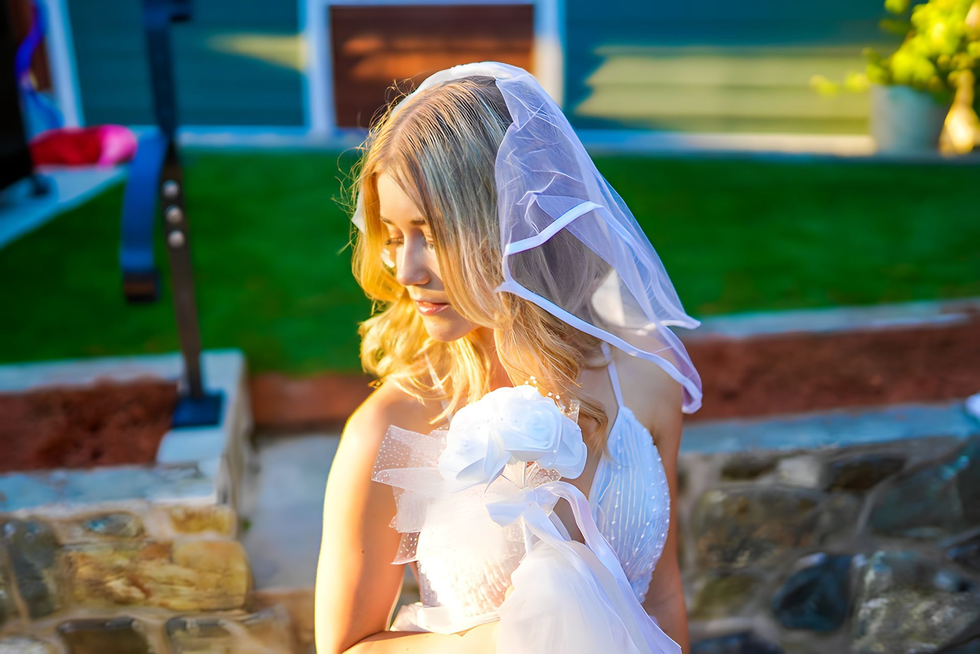 A woman in a wedding dress and veil is sitting on a rock.