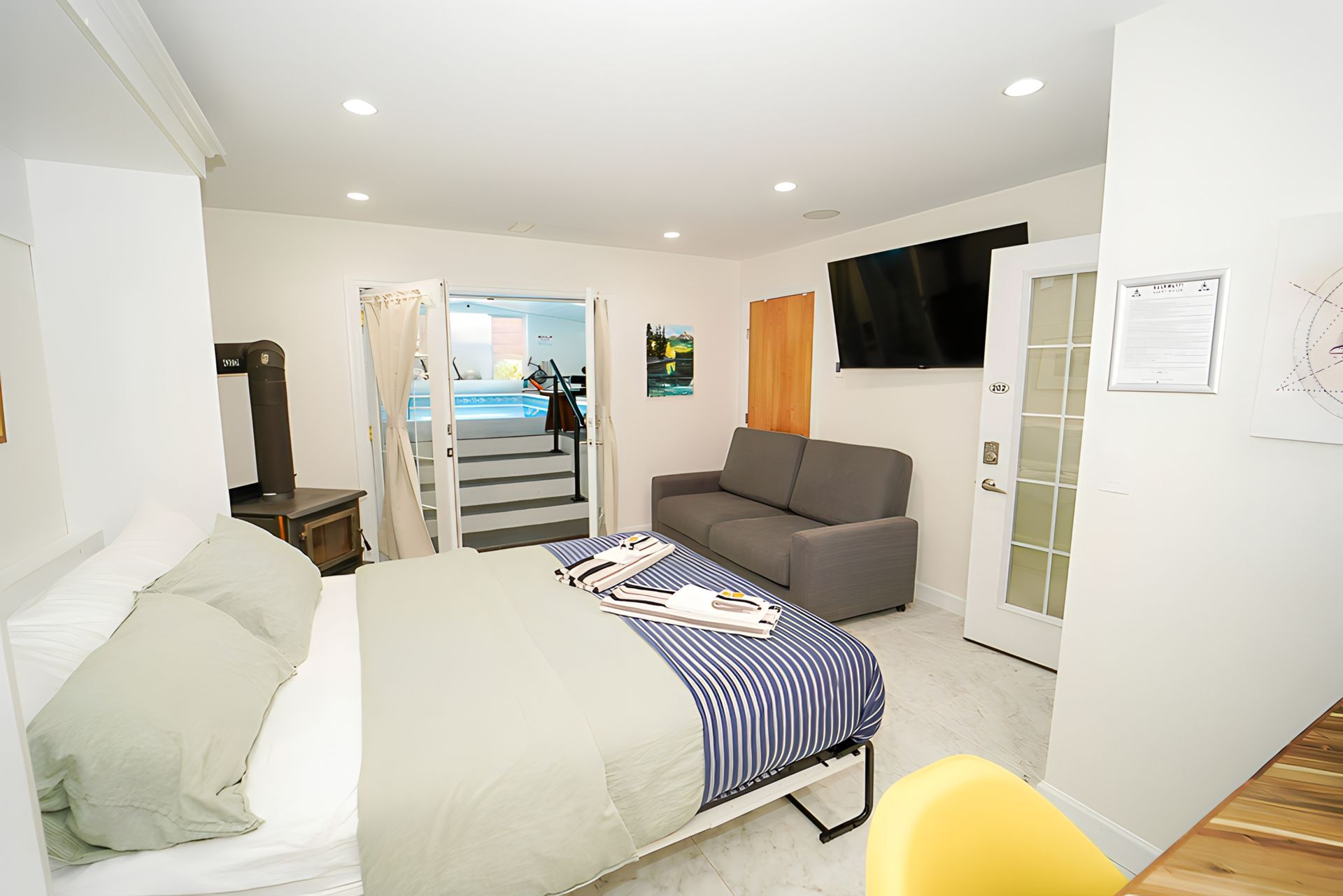 A small, bright room with a bed, sofa, TV, and access to a pool area.