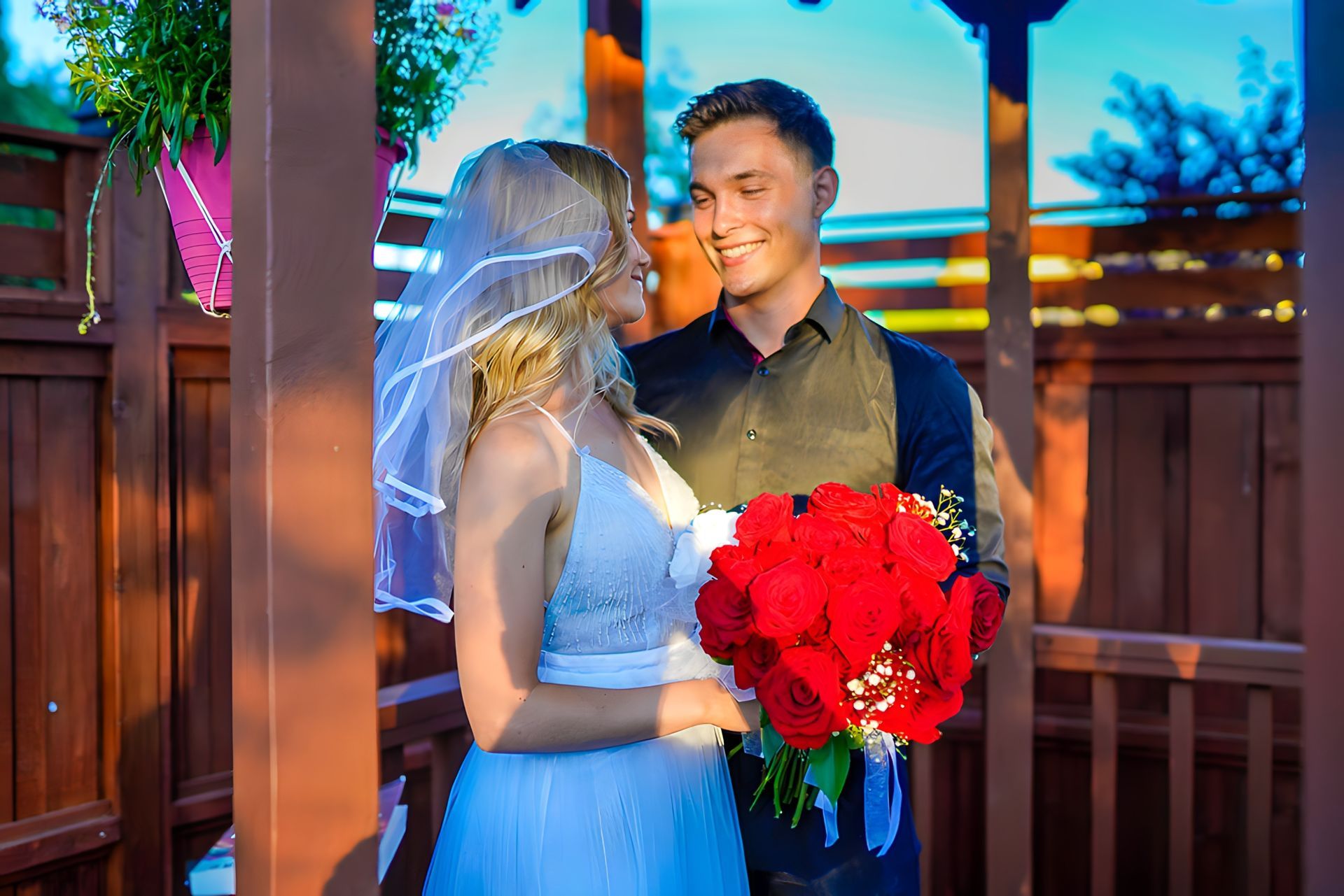 A bride and groom are standing next to each other holding a bouquet of red roses.