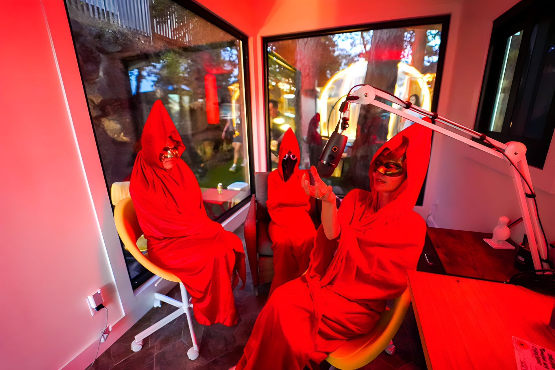 Two people in red robes are sitting in front of a microphone in a room.