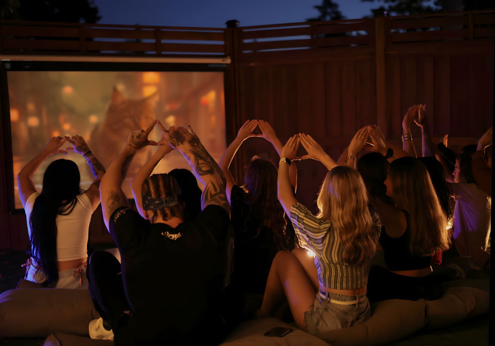 A group of people are sitting in front of a projector screen making a heart shape with their hands.