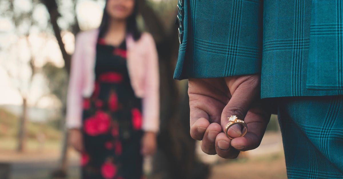 A man is holding a ring behind his back in front of a woman.
