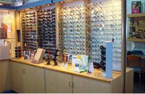 Exhibidor de gafas en una tienda, con muchas monturas en los estantes. Vitrinas beige debajo.