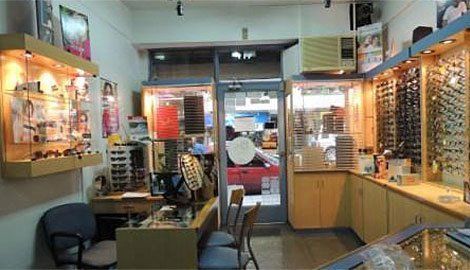 Interior de una óptica con gafas expuestas. Se ve un coche rojo a través de la puerta abierta.