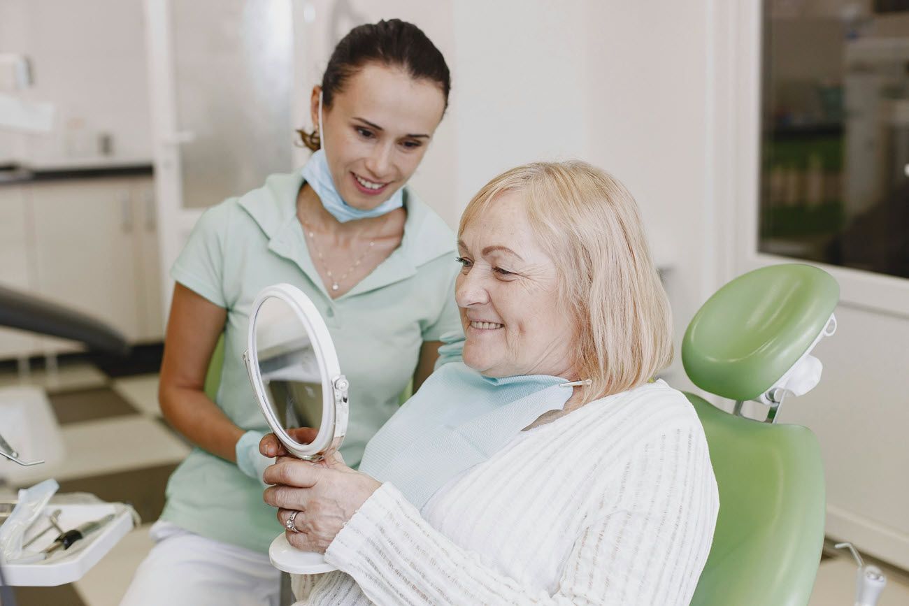 Dentist showing a smiling older woman her teeth in a mirror at a dental office.
