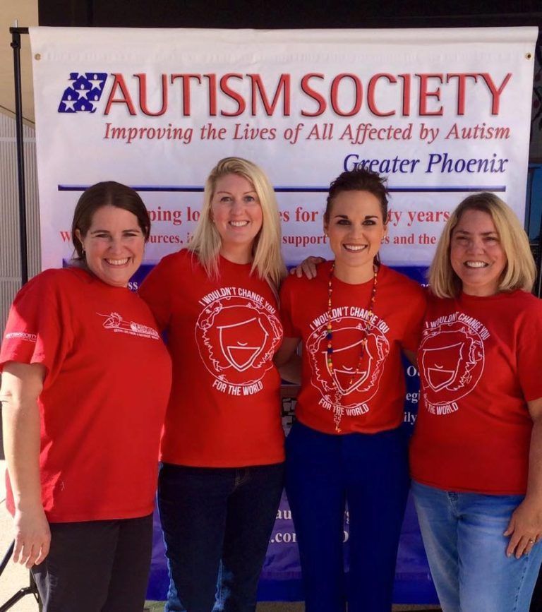 Four women wearing red t-shirts pose at a conference for Autism awareness.