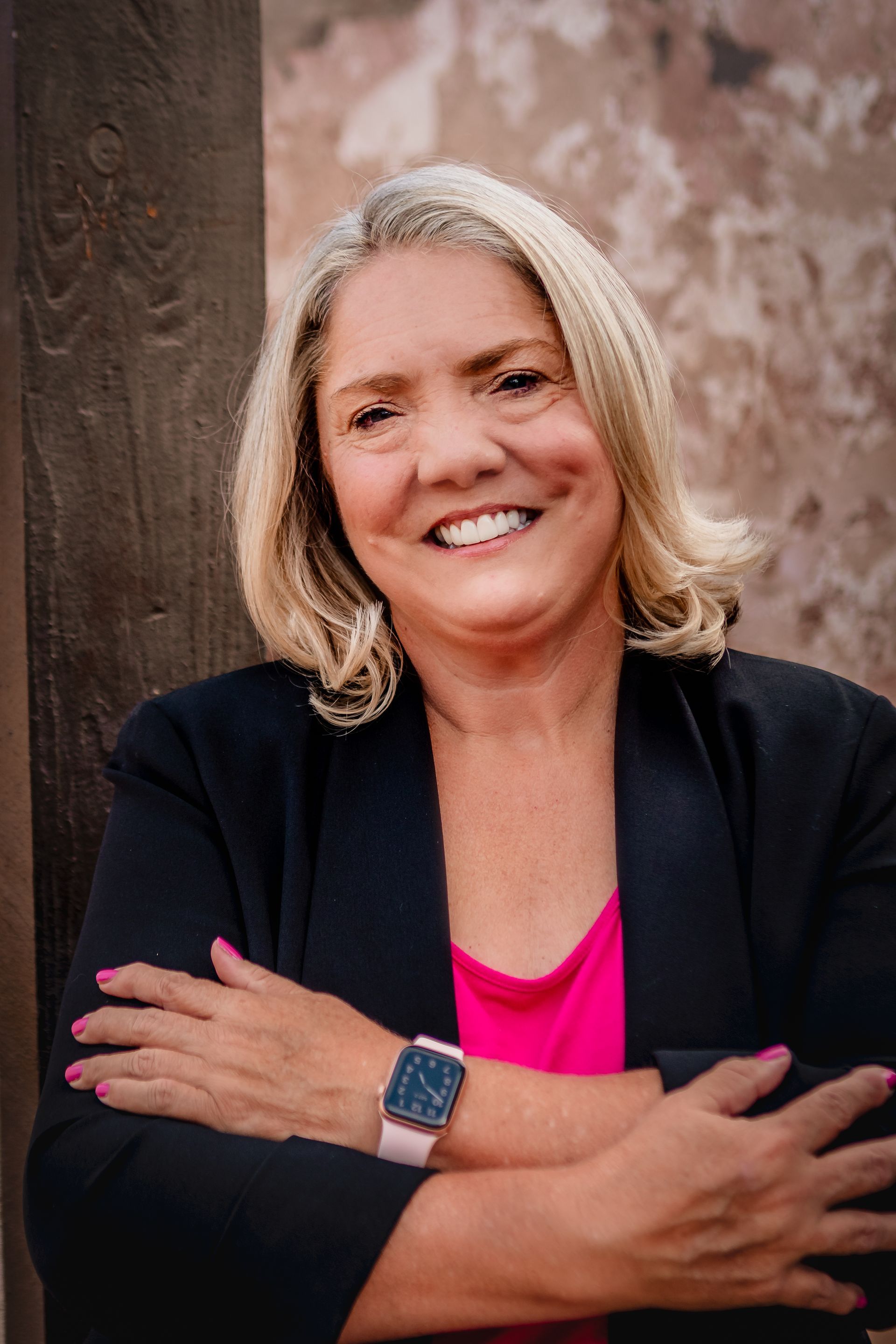 Agency founder Cynthia Macluskie, wearing a black jacket and a pink shirt, is smiling and standing with her arms crossed.