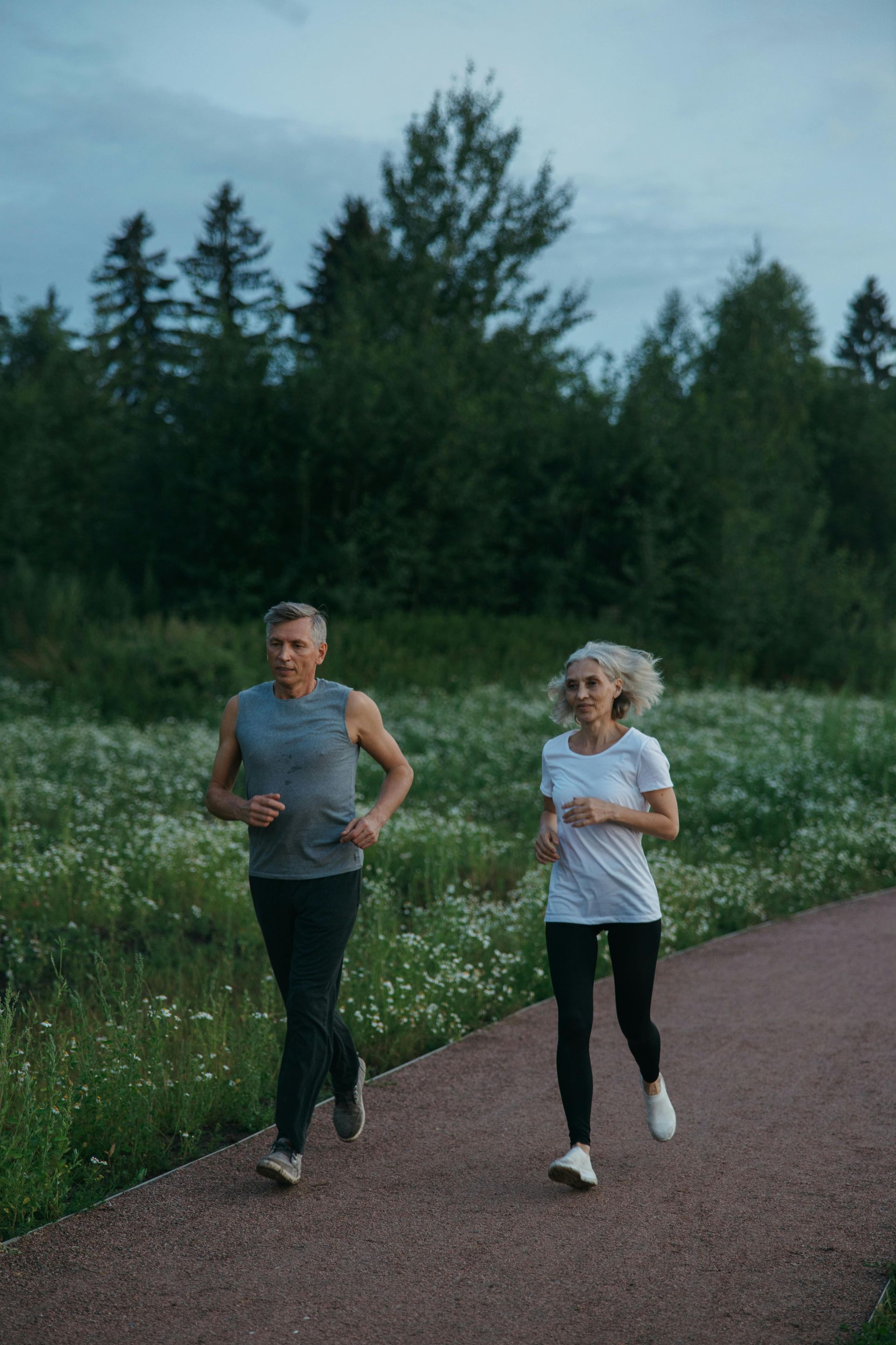 A man and a woman are jogging on a path in a park.