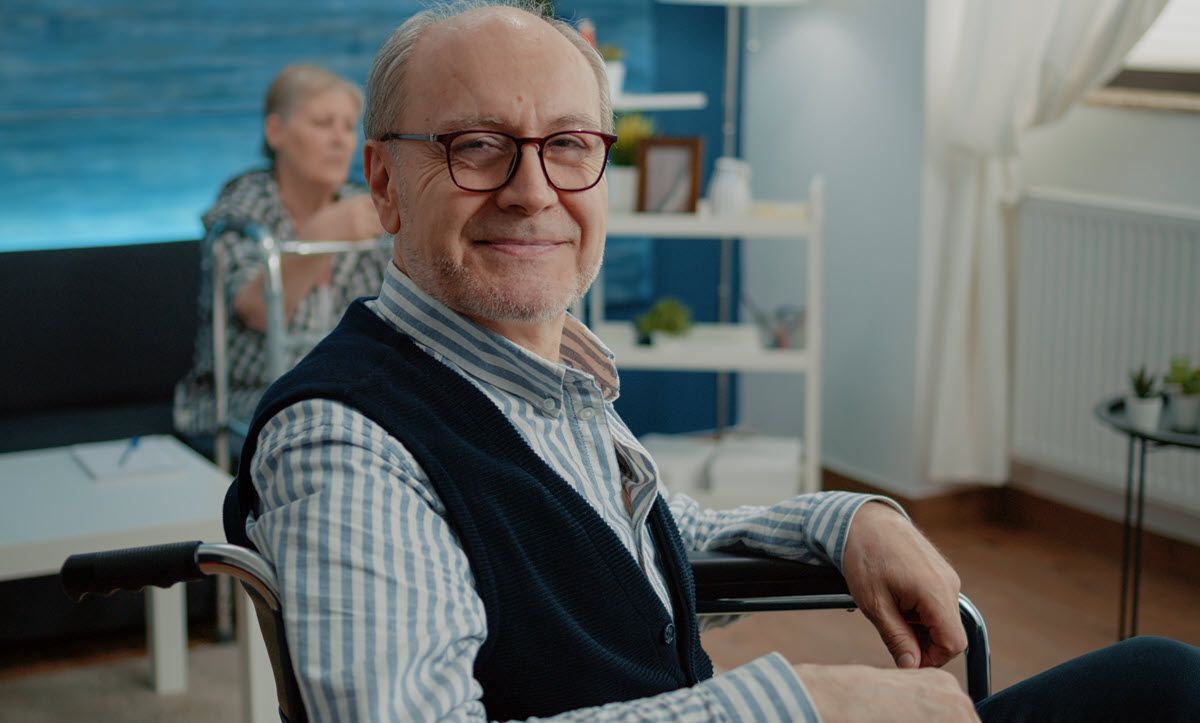 An elderly man is sitting in a wheelchair in a living room.