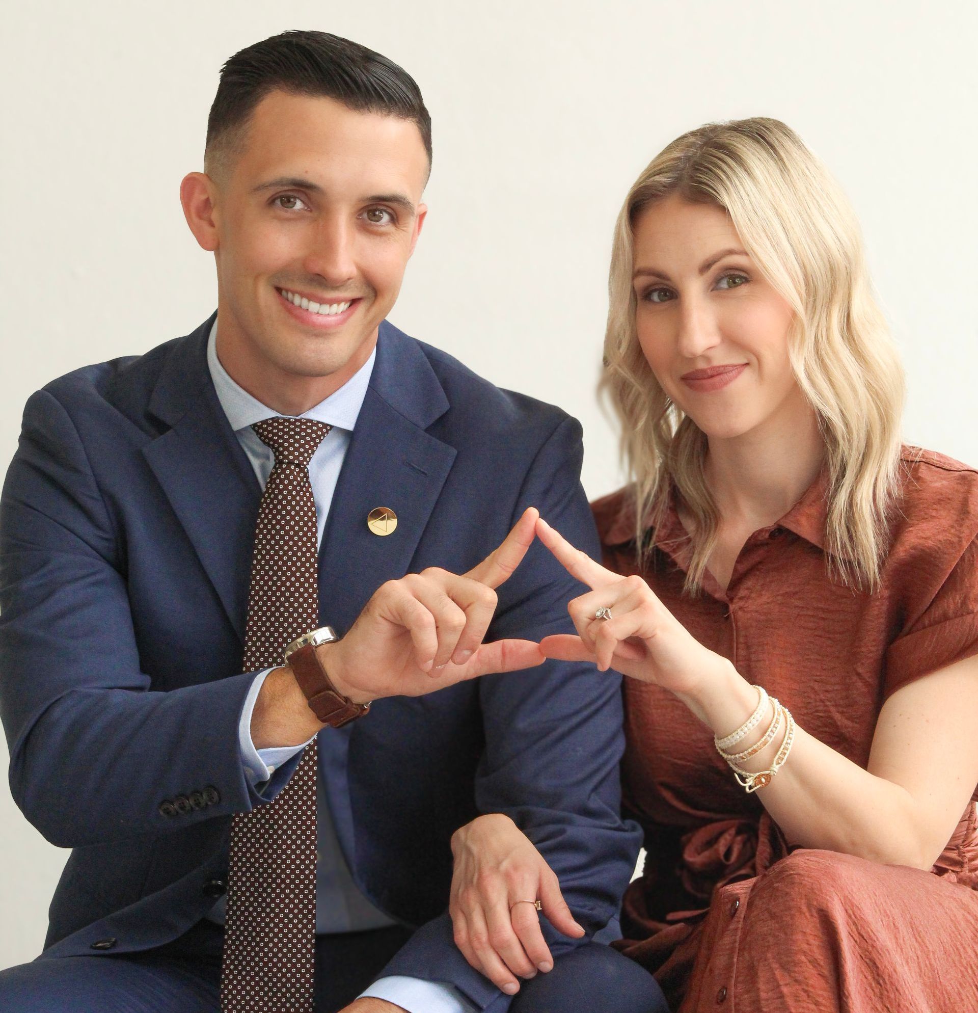 A man and a woman are sitting next to each other and making a heart shape with their hands