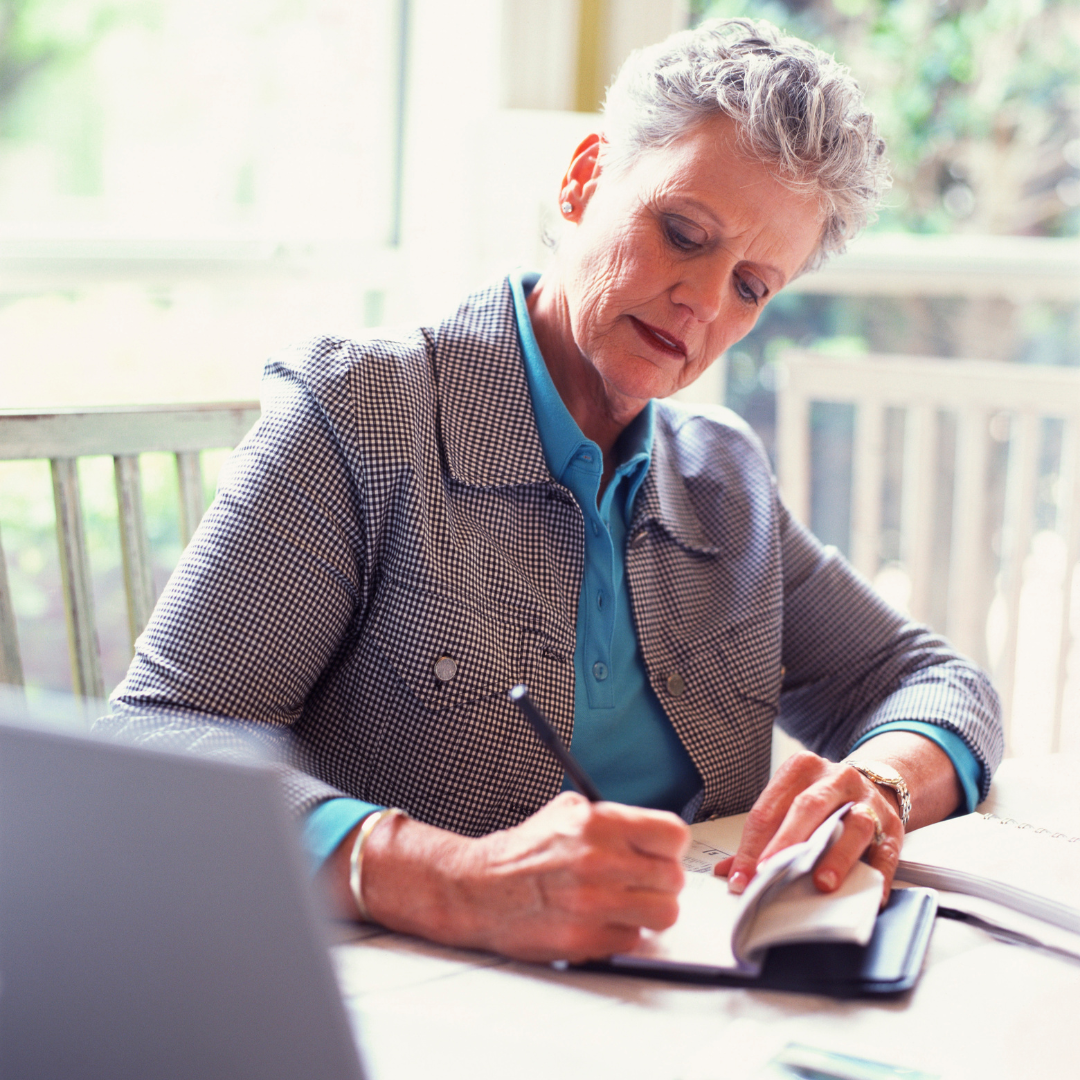 A woman is sitting at a table writing in a notebook