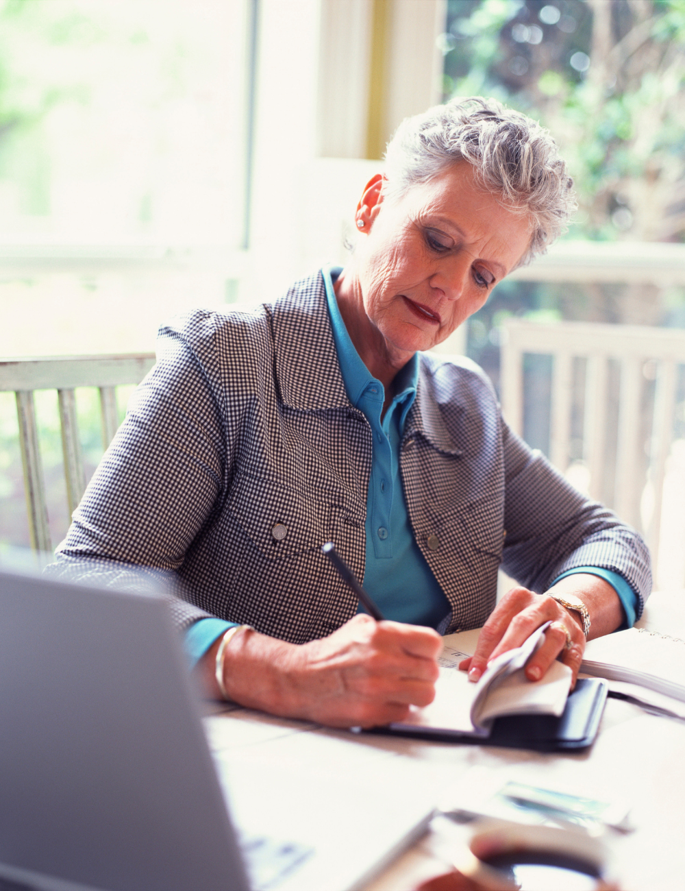An older woman is sitting at a desk writing in a notebook