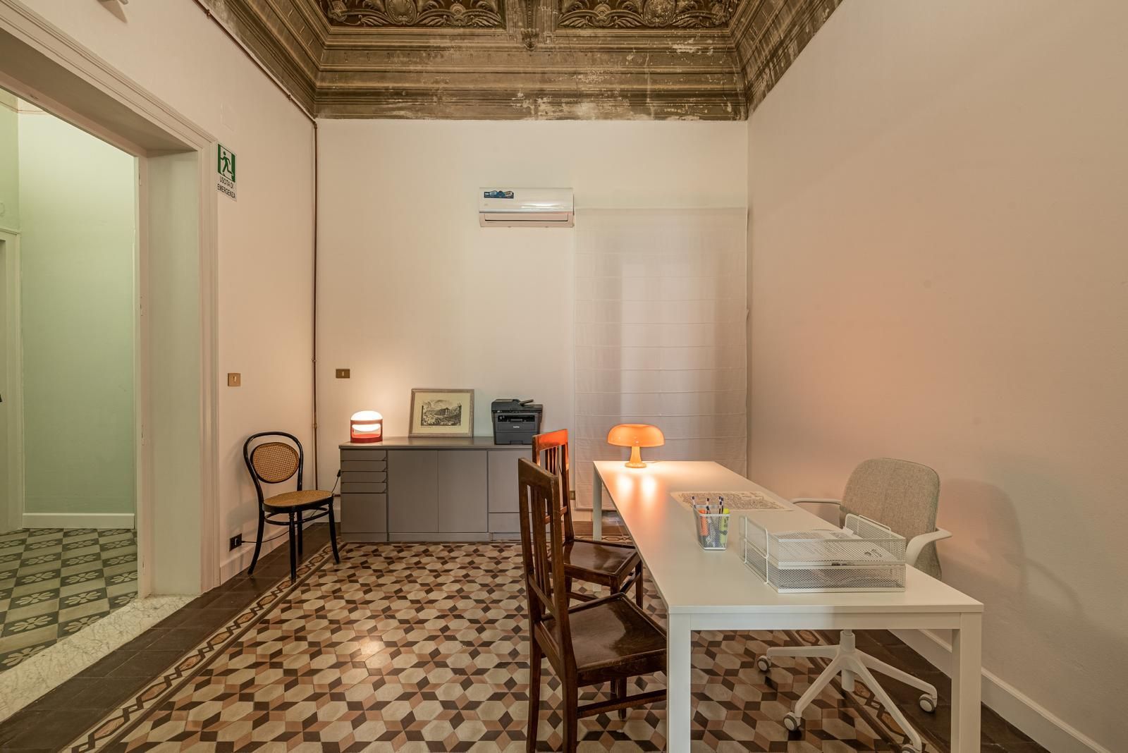 Ufficio con soffitto decorato, pavimento decorato, scrivania bianca, sedie e porta aperta sul corridoio.