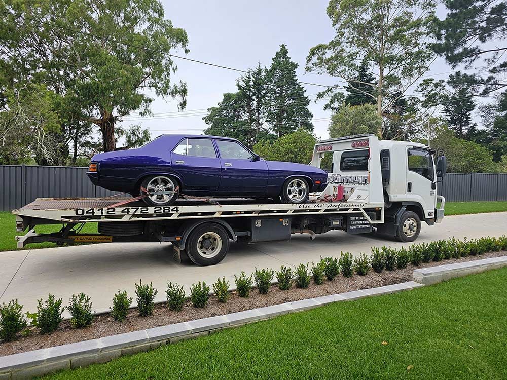 A Blue Car Is Being Towed By A Tow Truck — Optimum Towing in Bomaderry, NSW