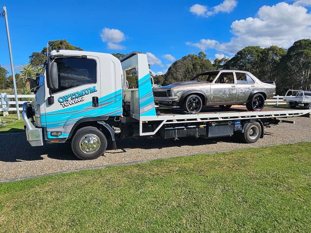 A Tow Truck is Carrying a Car on the Back of It — Optimum Towing in Kiama, NSW