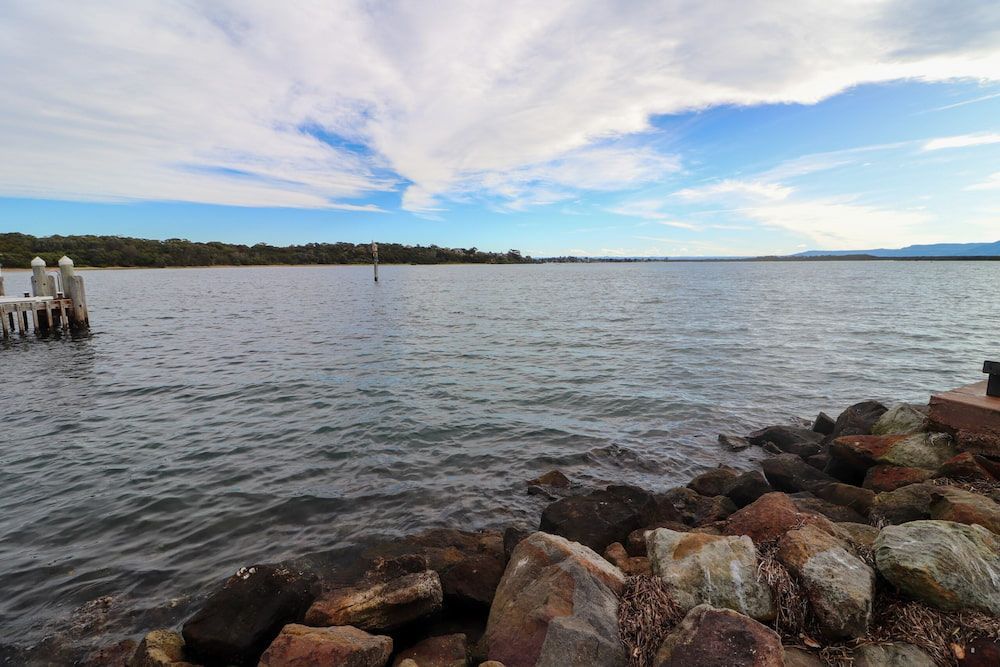 A Large Body of Water With Rocks in the Foreground and a Dock in the Background — Optimum Towing in Culburra Beach, NSW