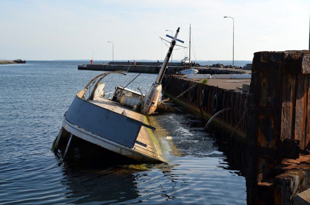A boat is floating on its side in the water near a dock.
