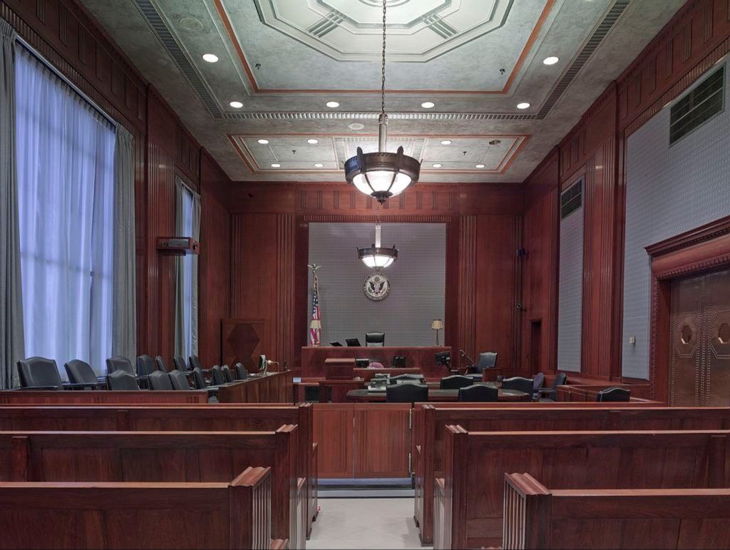 An empty courtroom with wooden benches and a chandelier hanging from the ceiling.