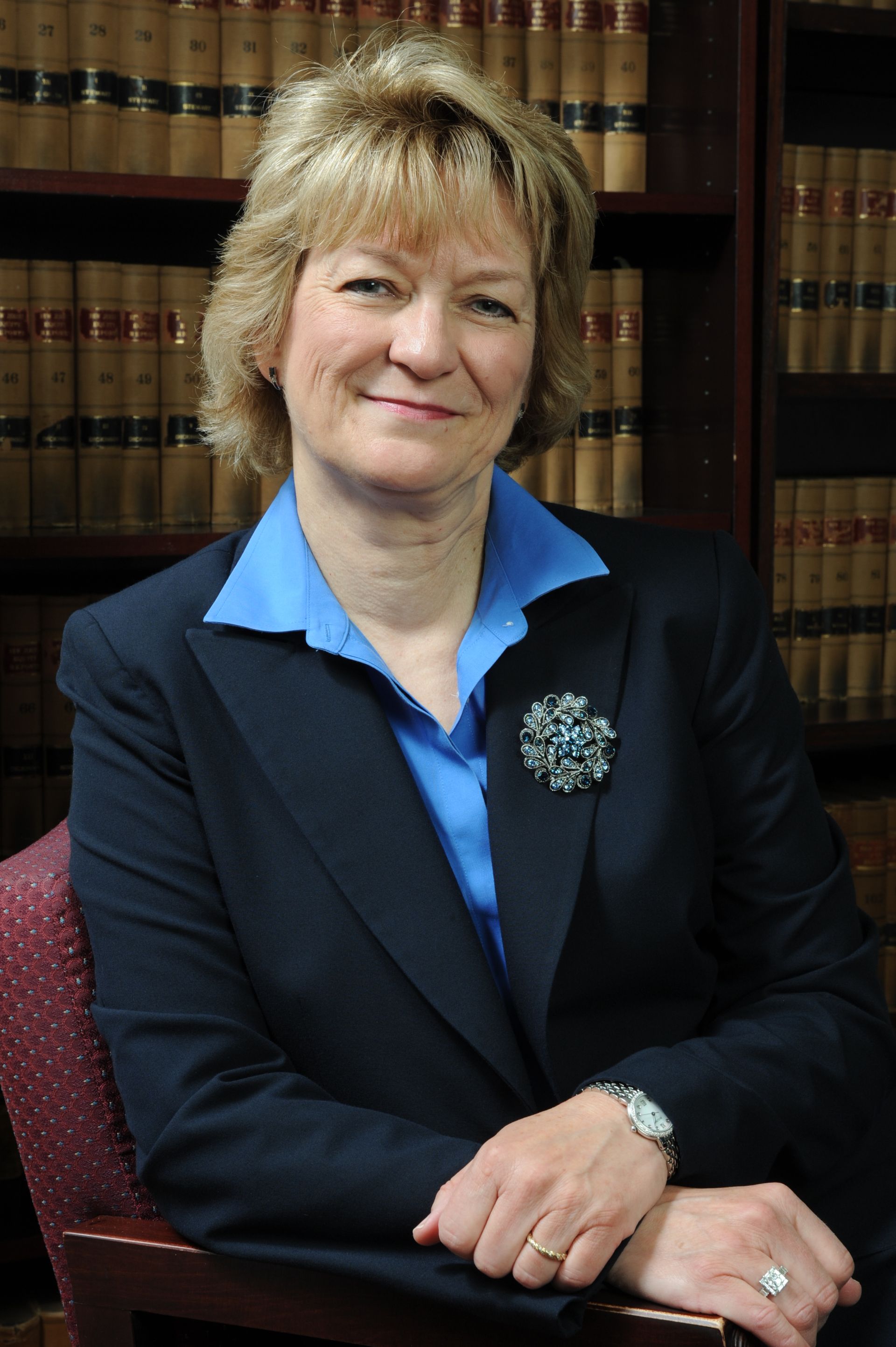 A woman in a suit is sitting in front of a bookshelf