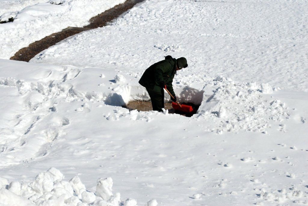A man is shoveling snow with a red shovel.