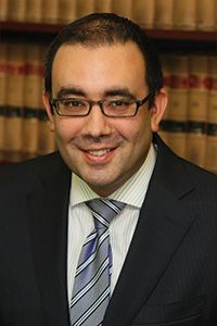 A man in a suit and tie is smiling in front of a bookshelf.