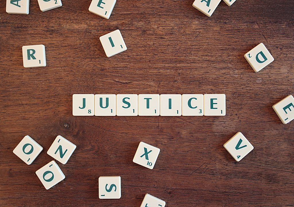 The word justice is written in scrabble tiles on a wooden table