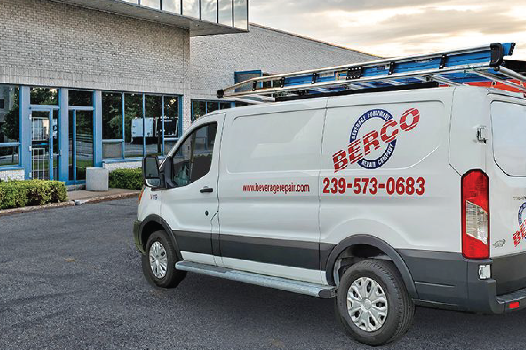 A white van with a ladder on top of it is parked in front of a building.