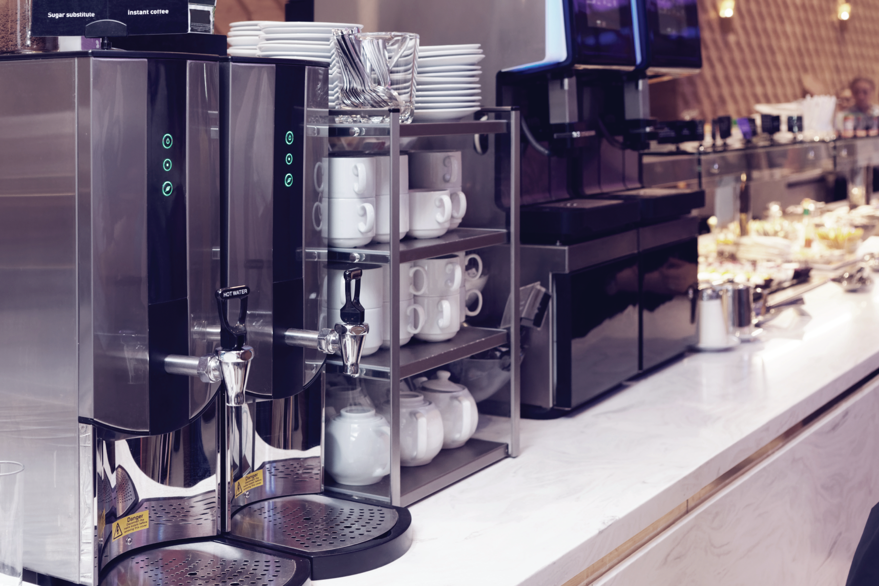 A kitchen with a lot of appliances and cups on a shelf.