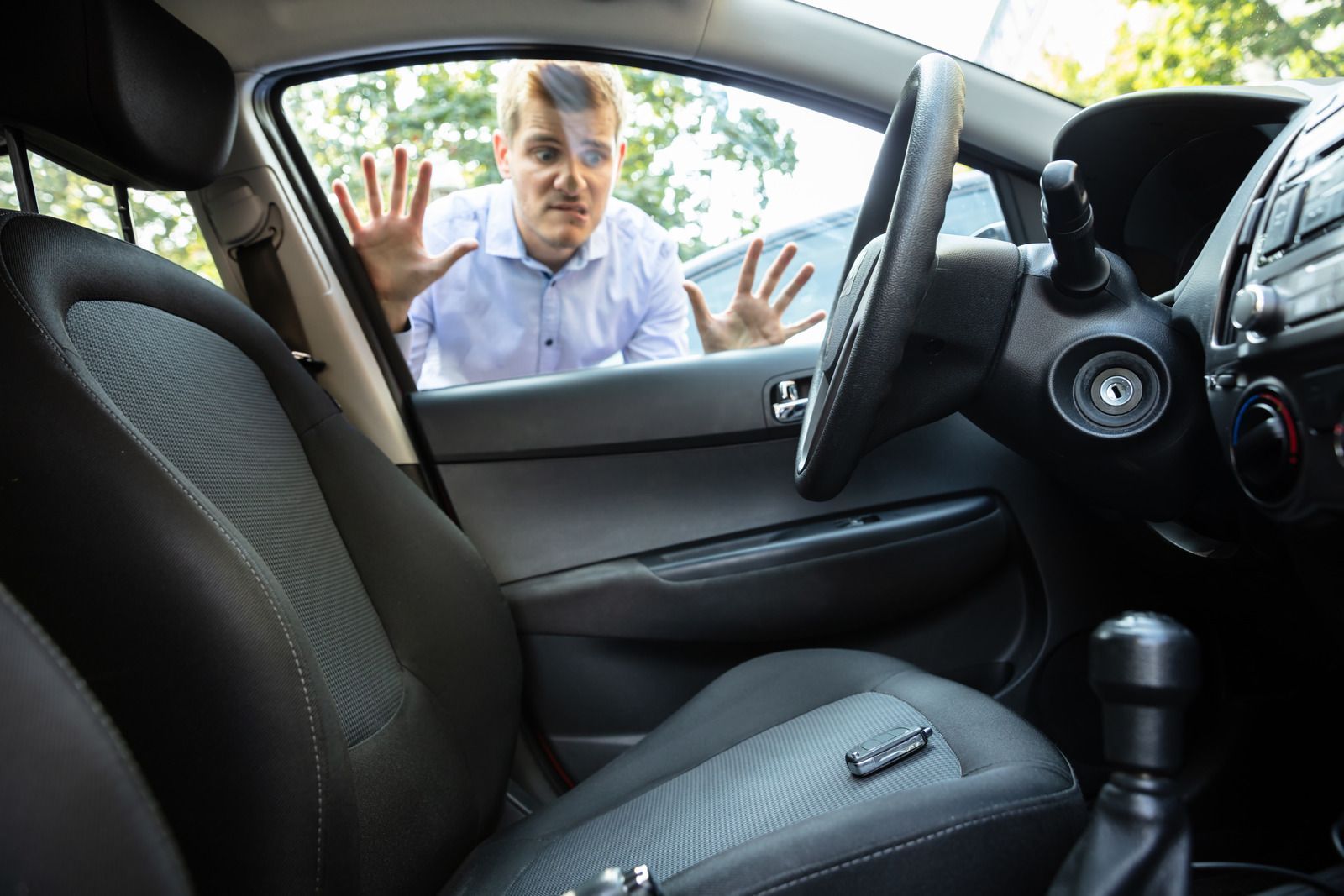 Man locked out of car, looking distressed, hands pressed against window, keys visible inside.