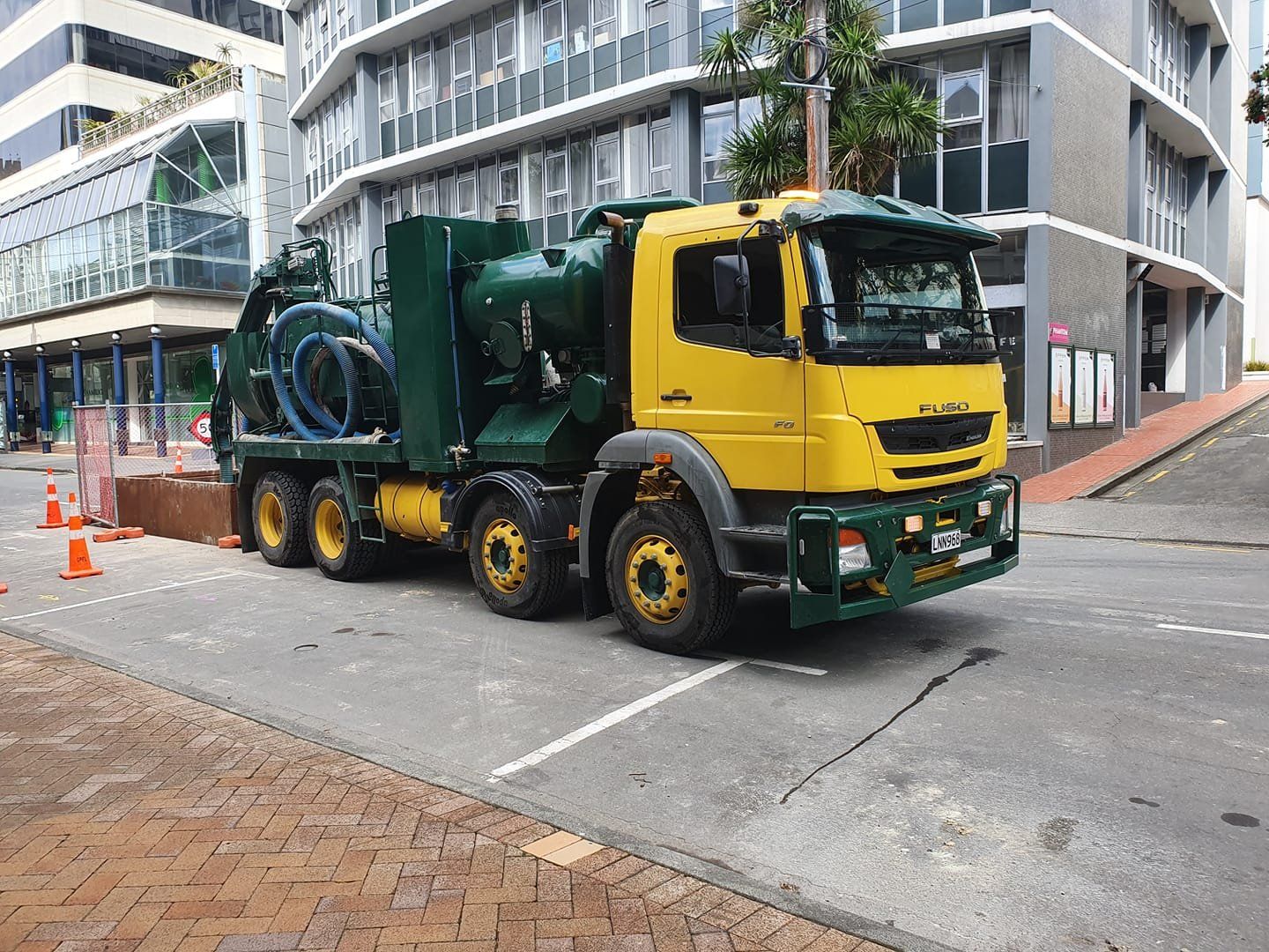 A yellow and green truck is parked on the side of the road in front of a building.