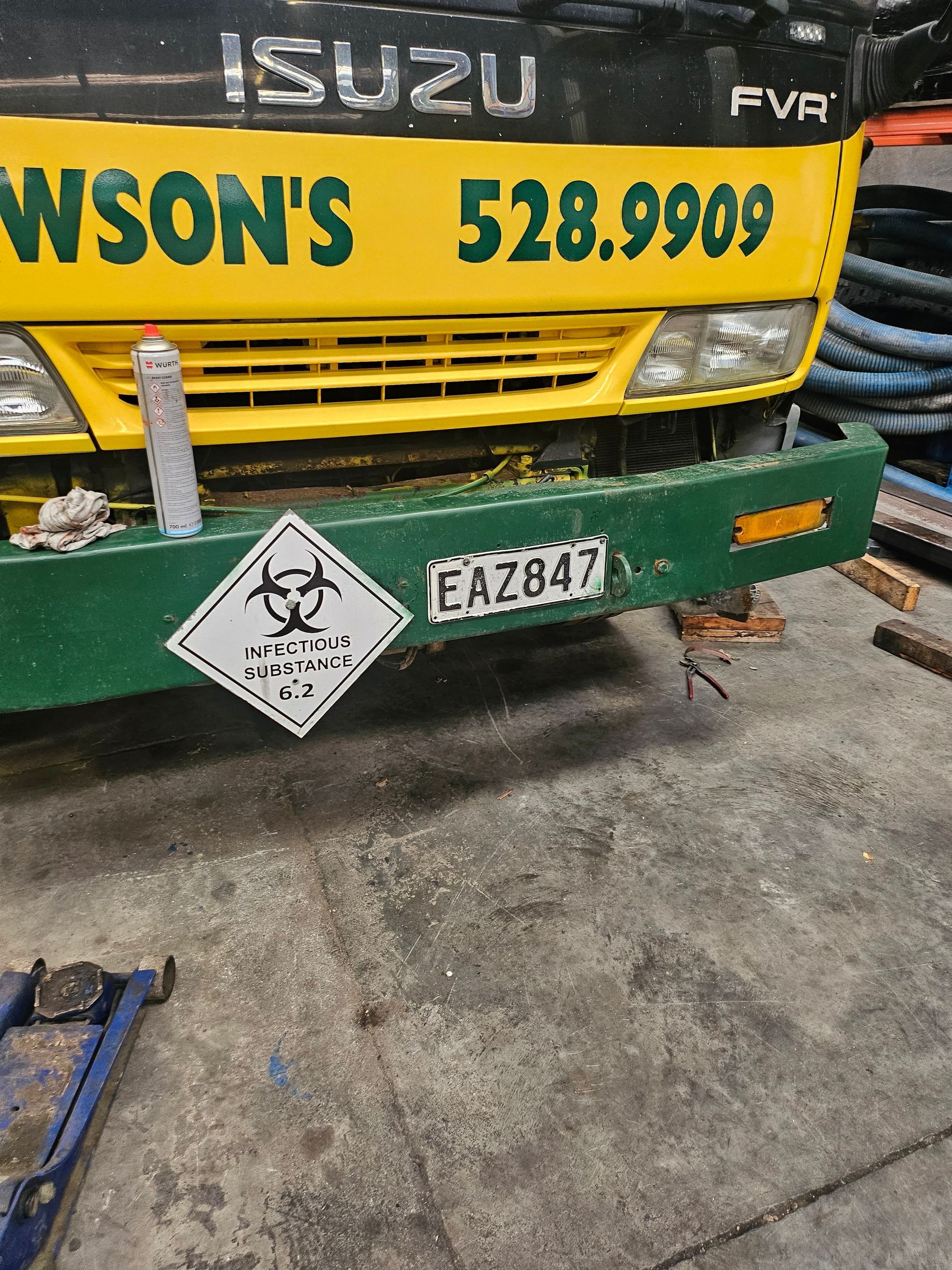 A yellow truck with a green bumper is parked in a garage.