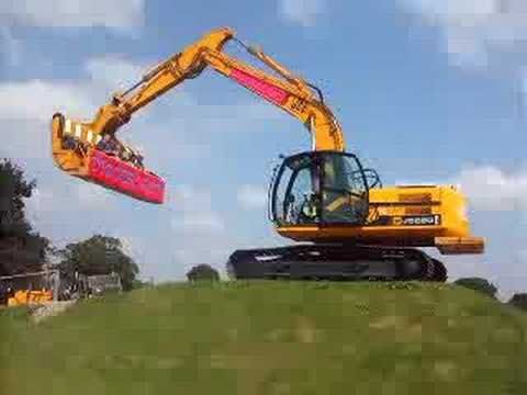 A yellow excavator is sitting on top of a grass covered hill.