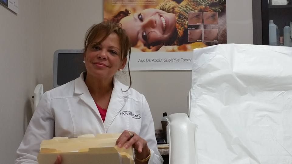 Woman in white coat, smiling, holding foam block in a medical office, with poster on wall.