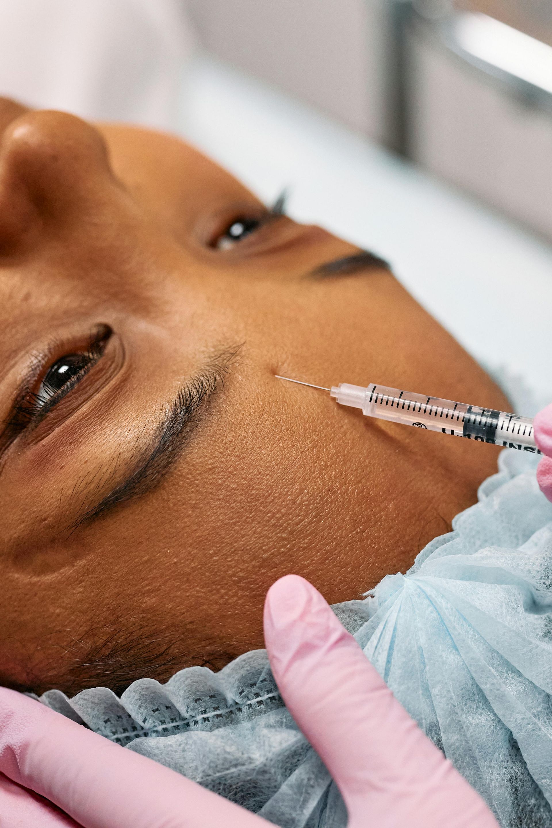 A person receiving a facial injection near the eye, in a medical setting.