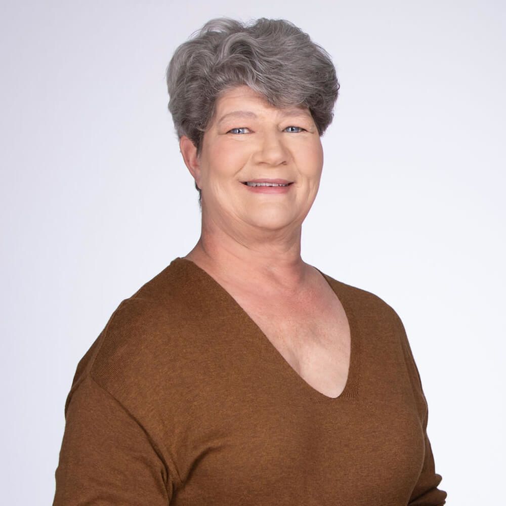 A woman in a brown sweater is smiling for the camera.