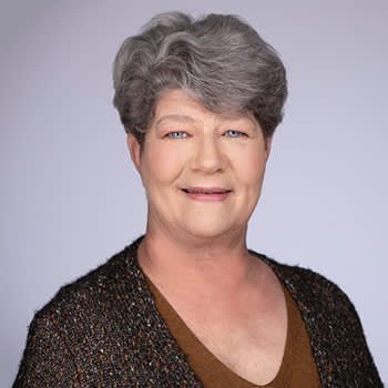 A woman with gray hair is wearing a brown shirt and a black sweater.