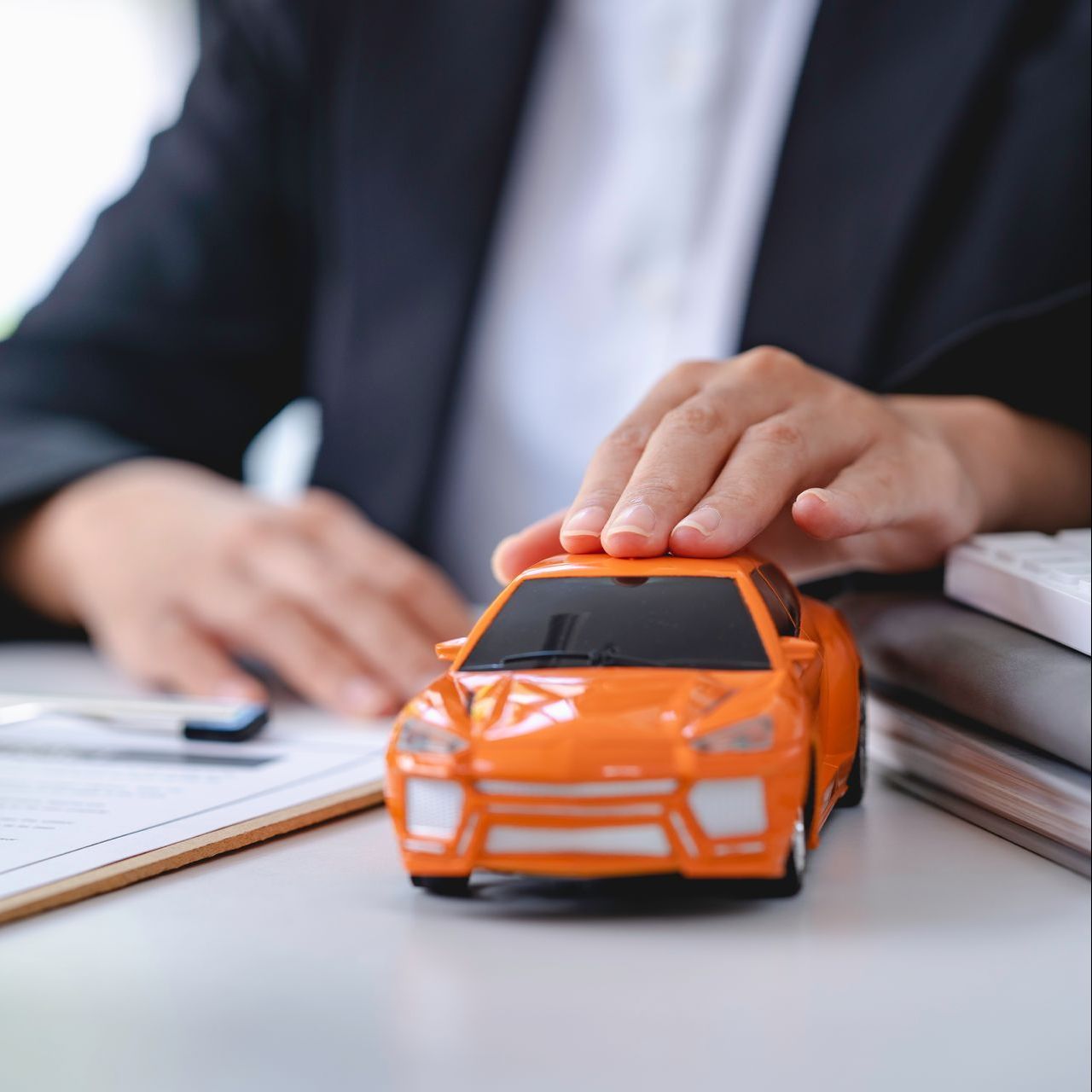 a man is holding an orange toy car in front of a clipboard