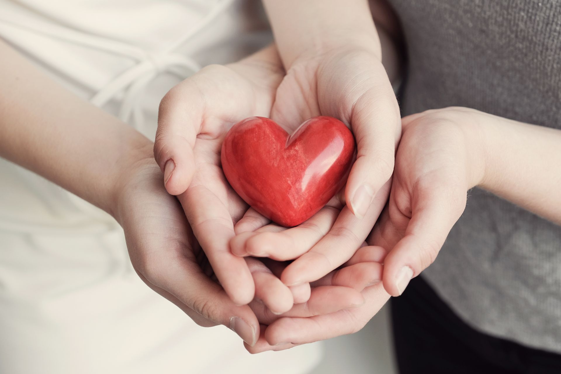 A woman and child are holding a red heart in their hands.