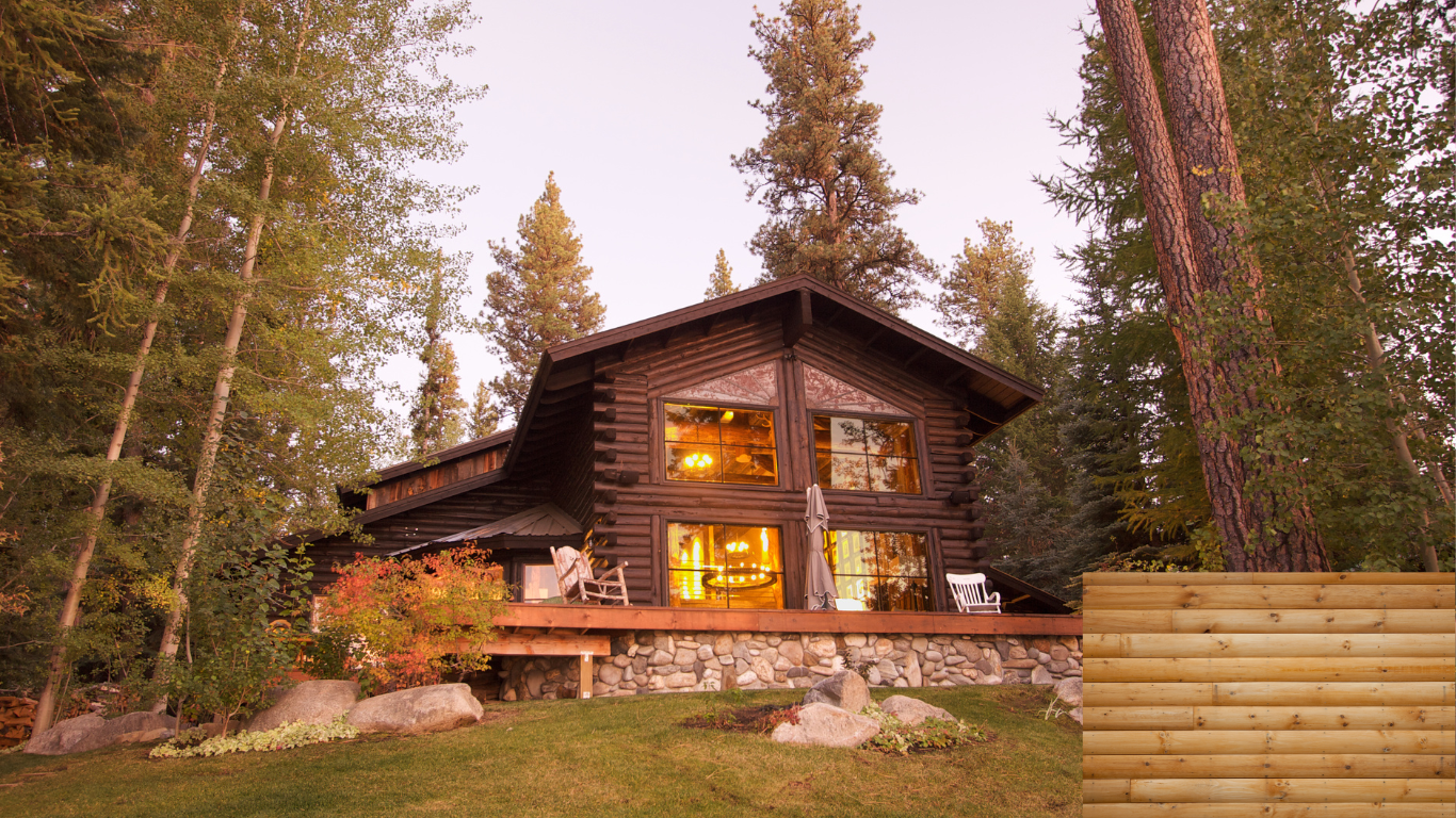 A log cabin is surrounded by trees and a wooden fence.