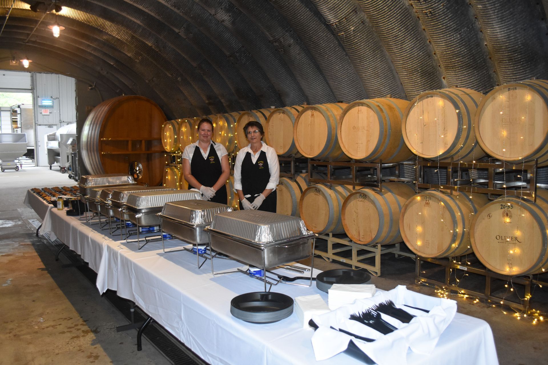 Buffet table set up in a barrel-lined wine cellar with two staff members standing behind it