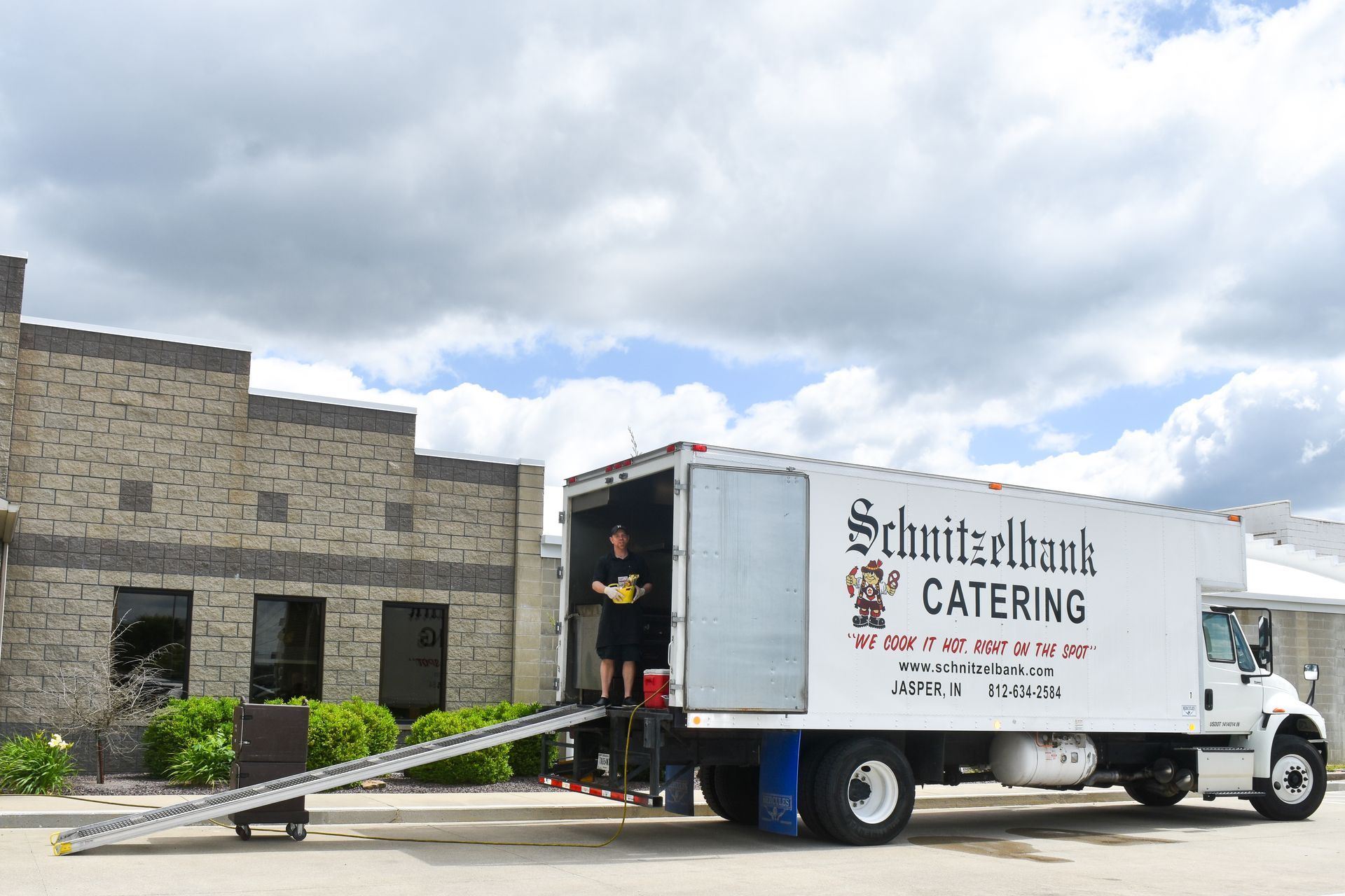 White catering truck parked at a stone building with a ramp, under a cloudy sky