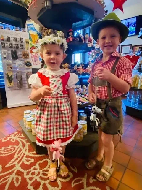 Two children in festive costumes and hats standing indoors on a tiled floor.