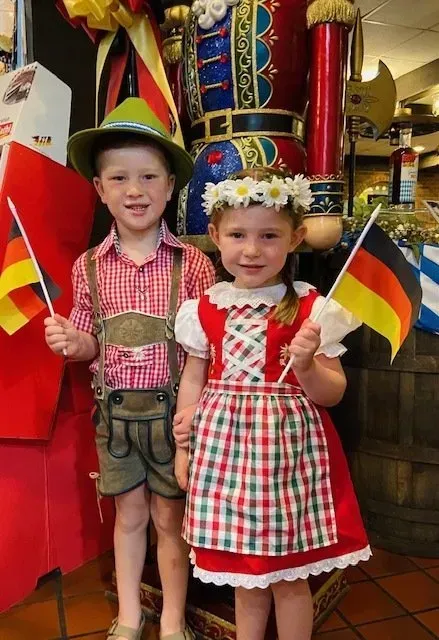 Two children in red checkered outfits waving small flags in a festive indoor setting