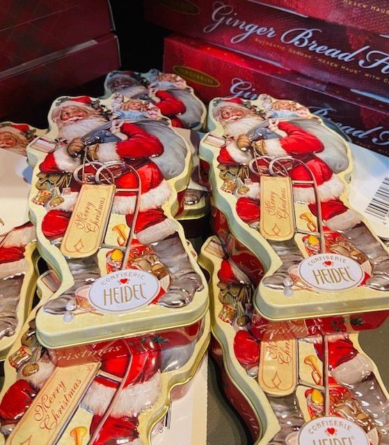 Red and gold Christmas gingerbread house gift boxes with candy decorations and name tags on a display shelf