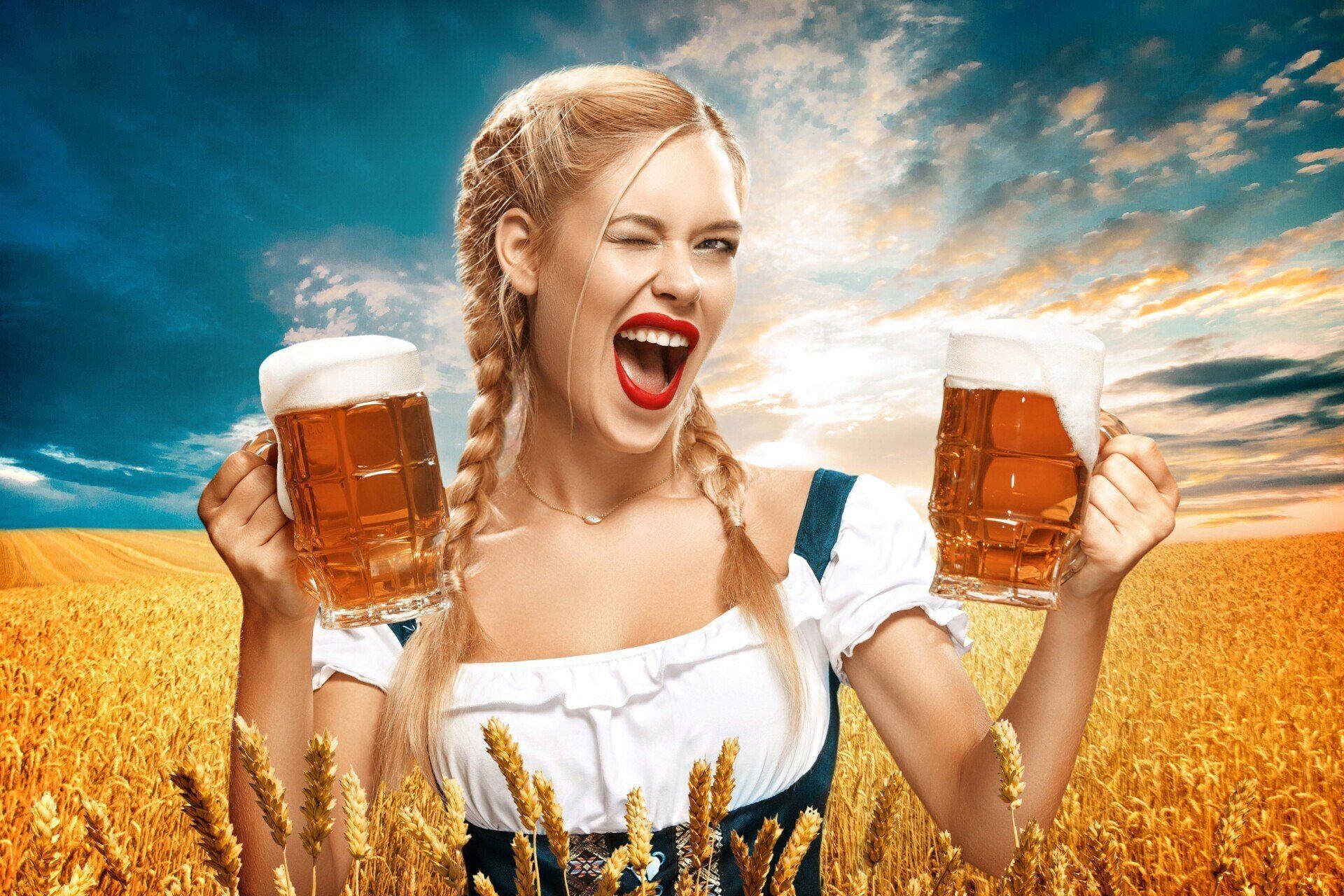 Woman cheering with two beer mugs in a wheat field under a bright blue sky