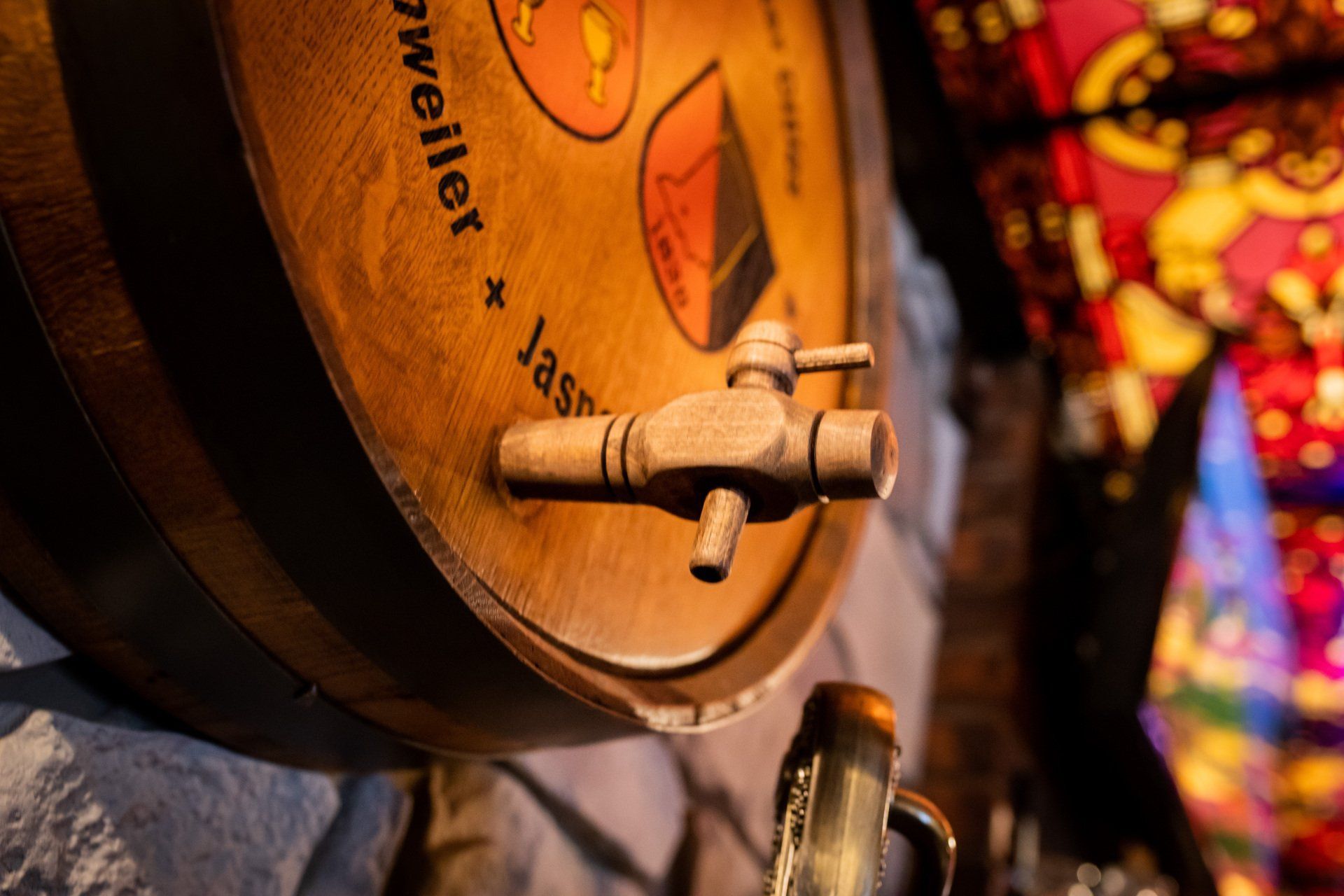 Close-up of a wooden barrel tap with orange labels and a warm, festive background